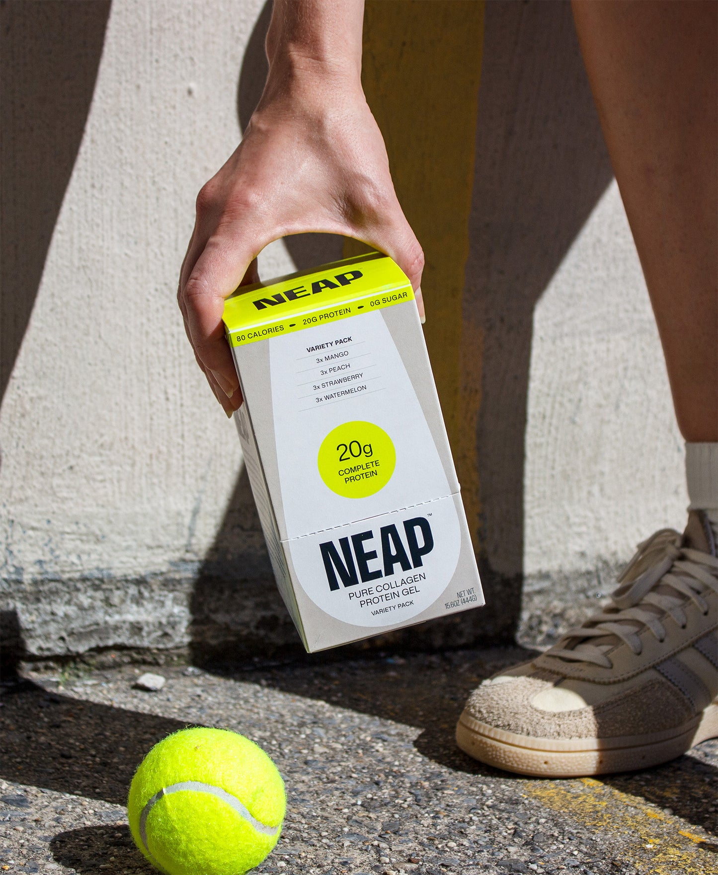 Person holding a NEAP protein packaging with a tennis ball on a concrete surface