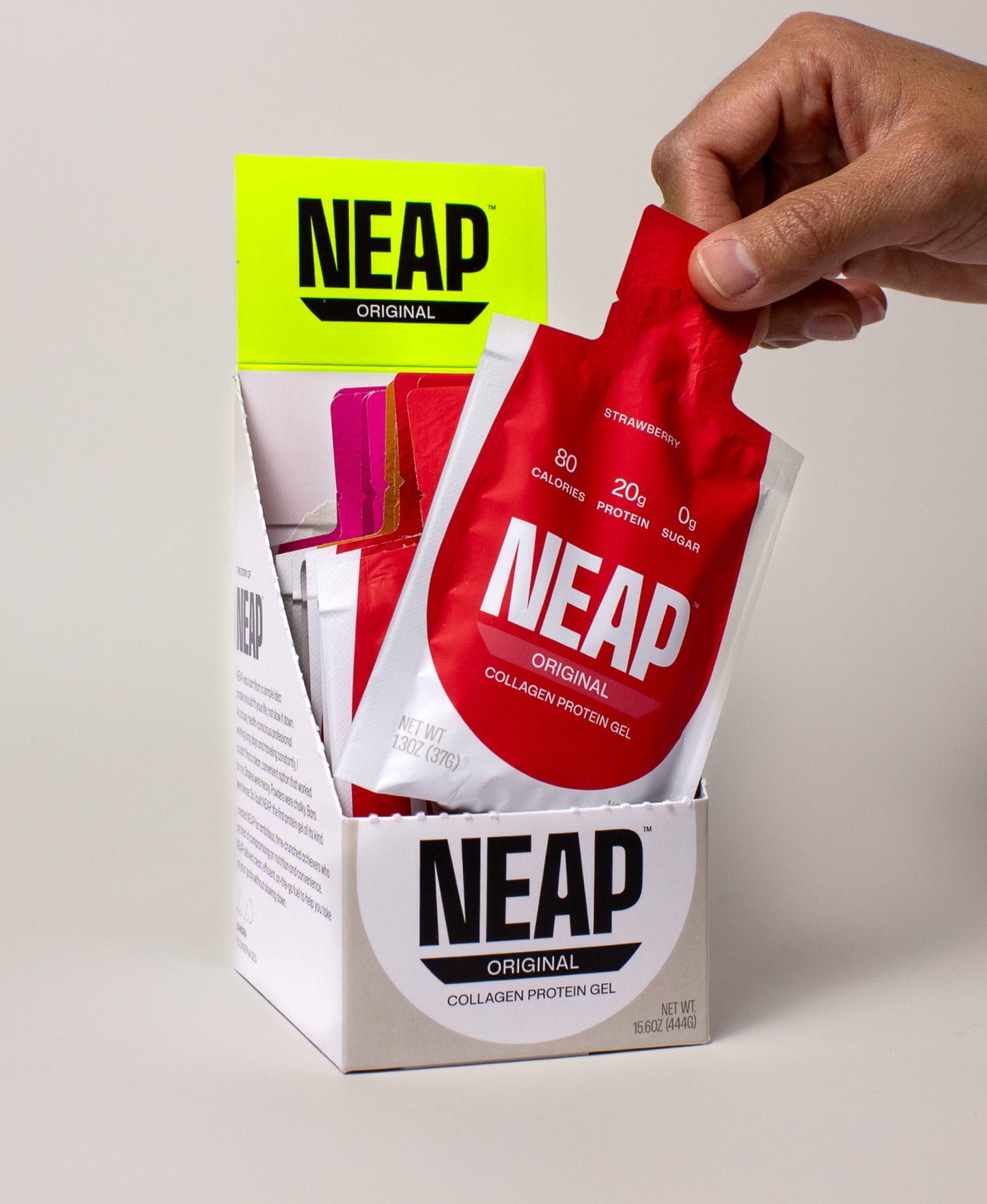 Hand grabbing a NEAP Original collagen protein gel packet out of NEAP Original Variety Box display box.