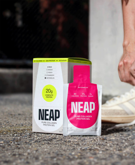 Watermelon NEAP protein gel pouch and box on a concrete tennis court with a person reaching for the box.
